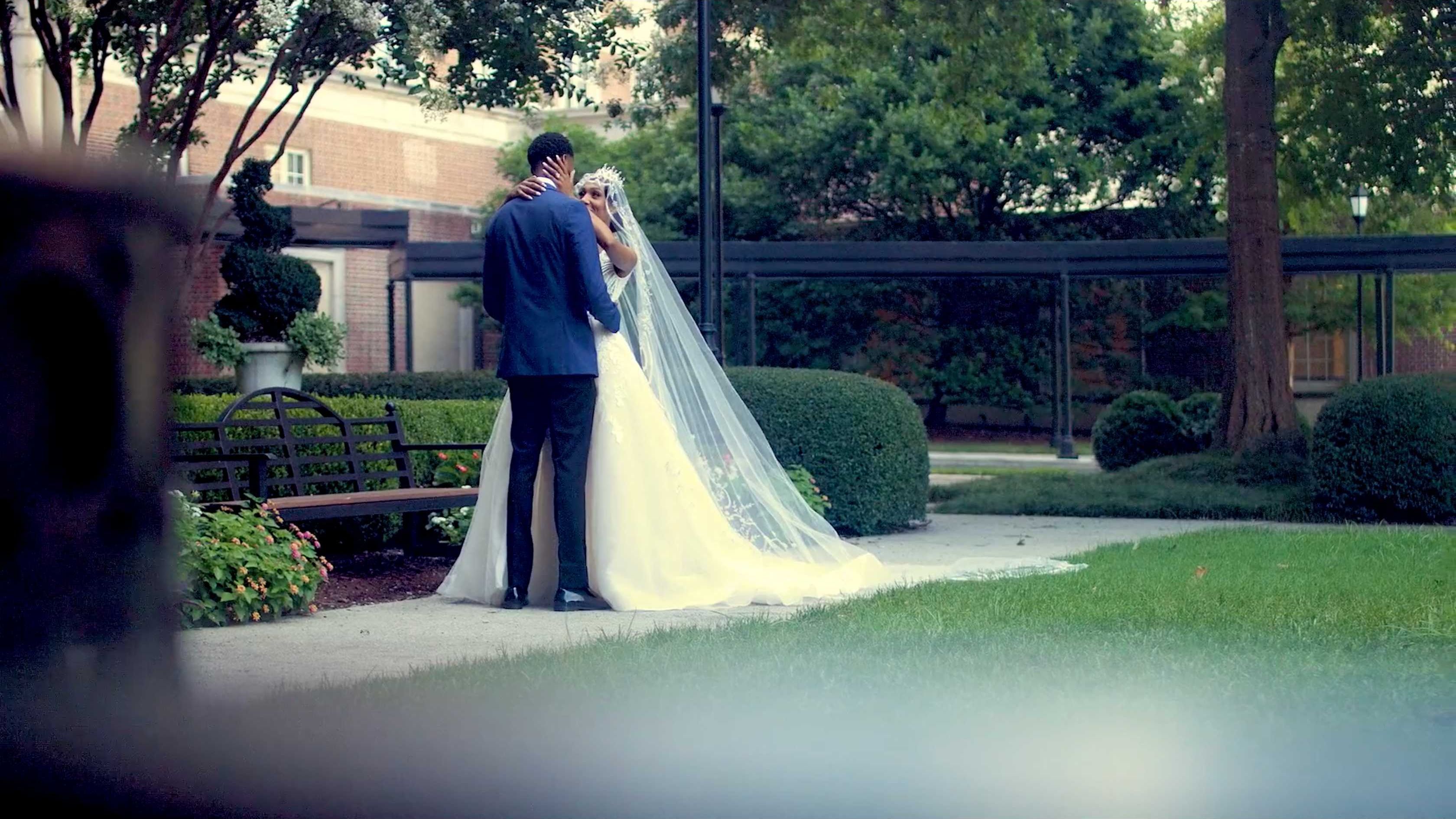 A bride and groom embracing in a formal garden, her long veil trailing across the path