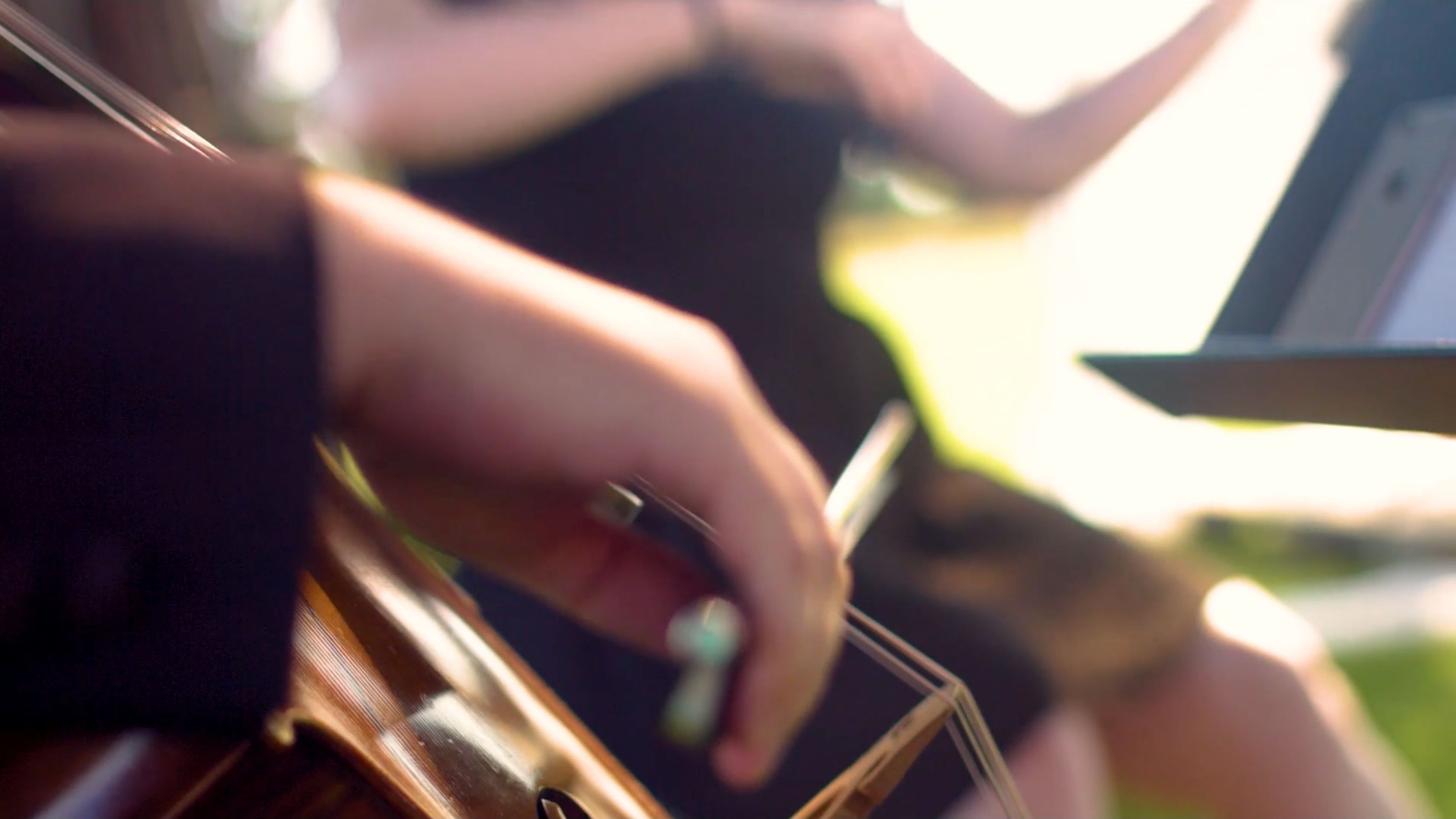 Close-up of a musician's hand bowing a string instrument in warm sunlight