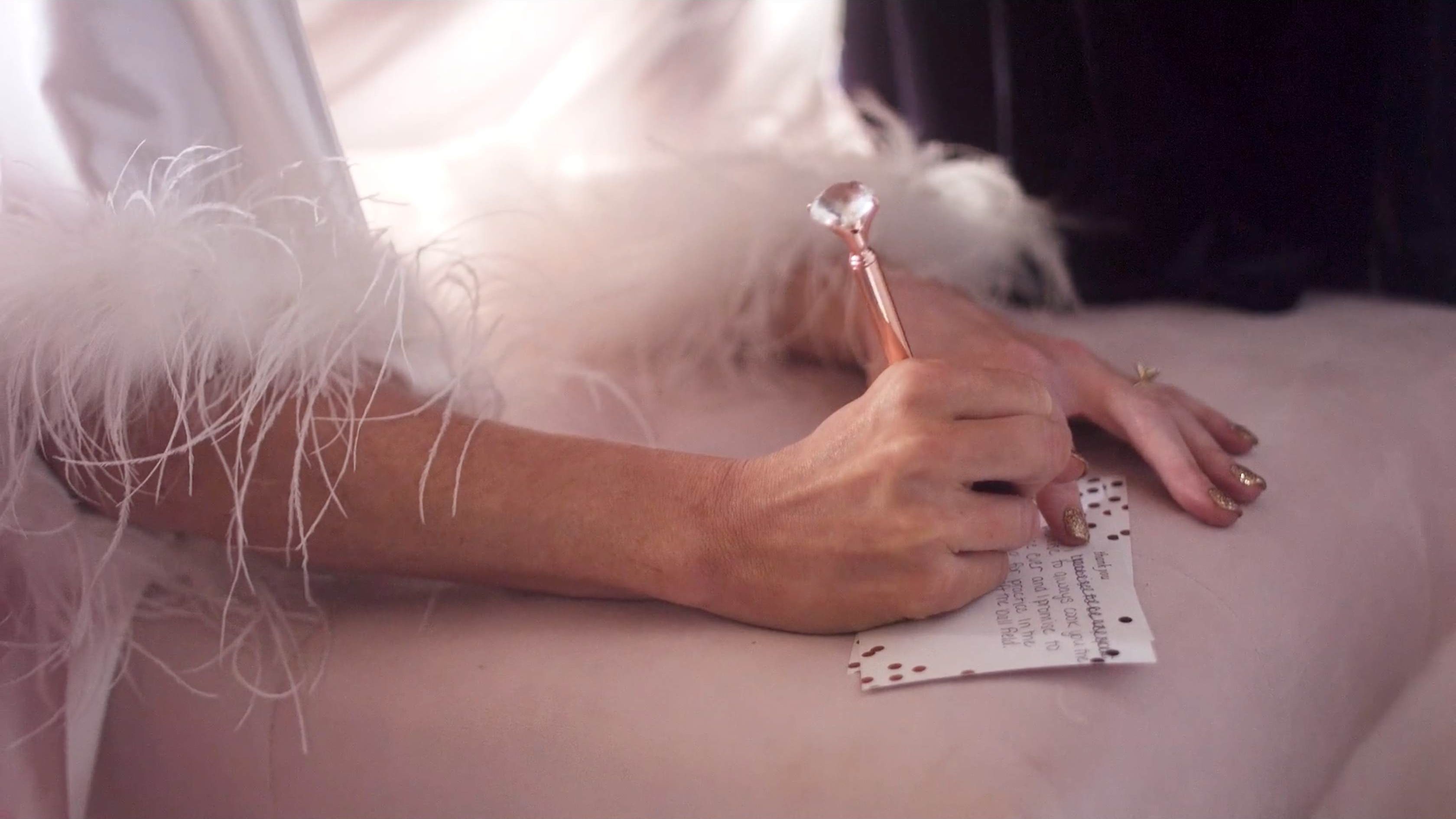 A bride writing a handwritten note with a rose-gold crystal pen